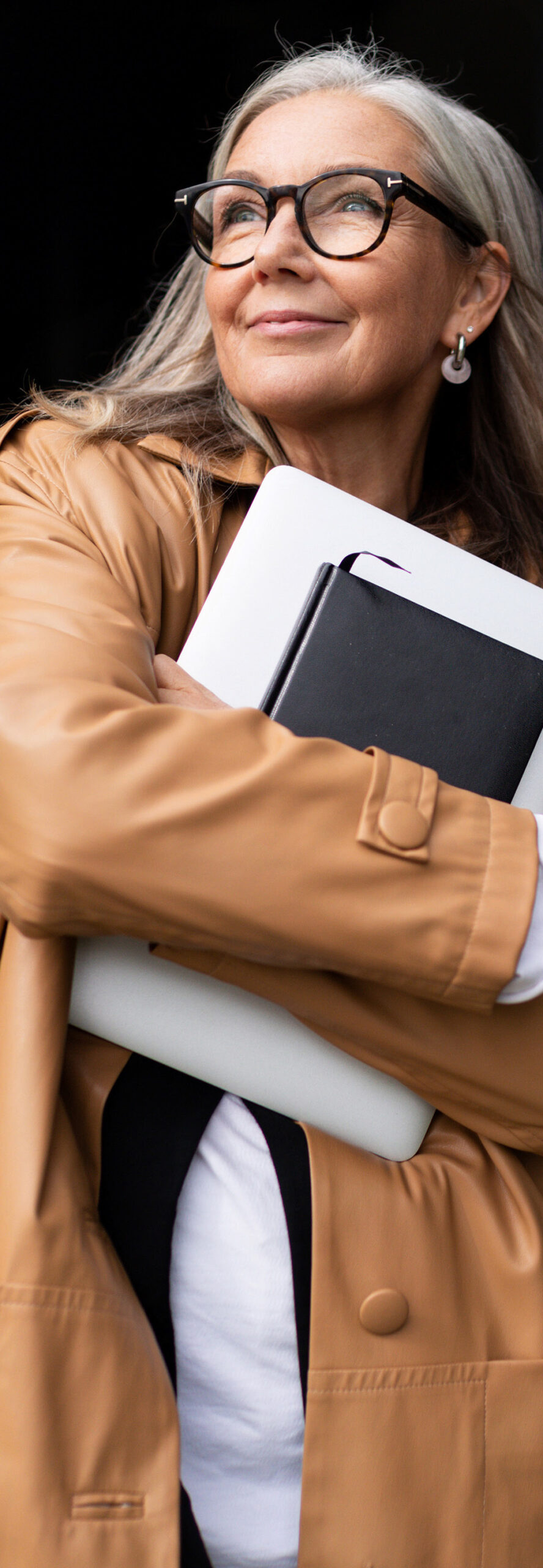 businesswoman in tan leather jacket with portfolio looking up left.